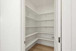 **DISCLAIMER** Interior package may vary. Spacious walk-in pantry featuring multiple levels of white shelving, wood-finish flooring, and a white interior door with a chrome knob