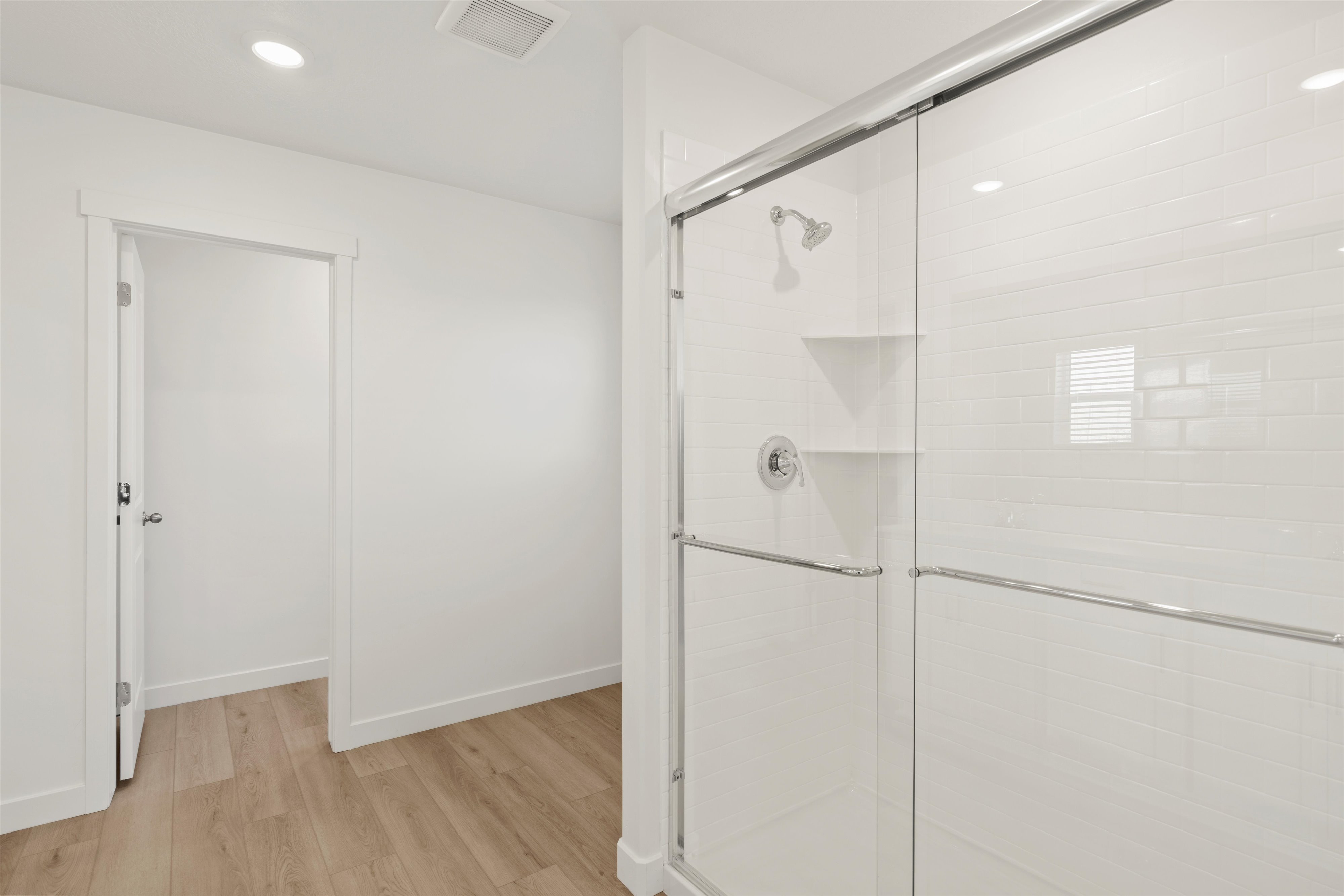 **DISCLAIMER** Interior package may vary. Shower enclosure featuring subway tile surround, glass sliding doors, built-in shelving, a rainfall showerhead, and a bright chrome faucet