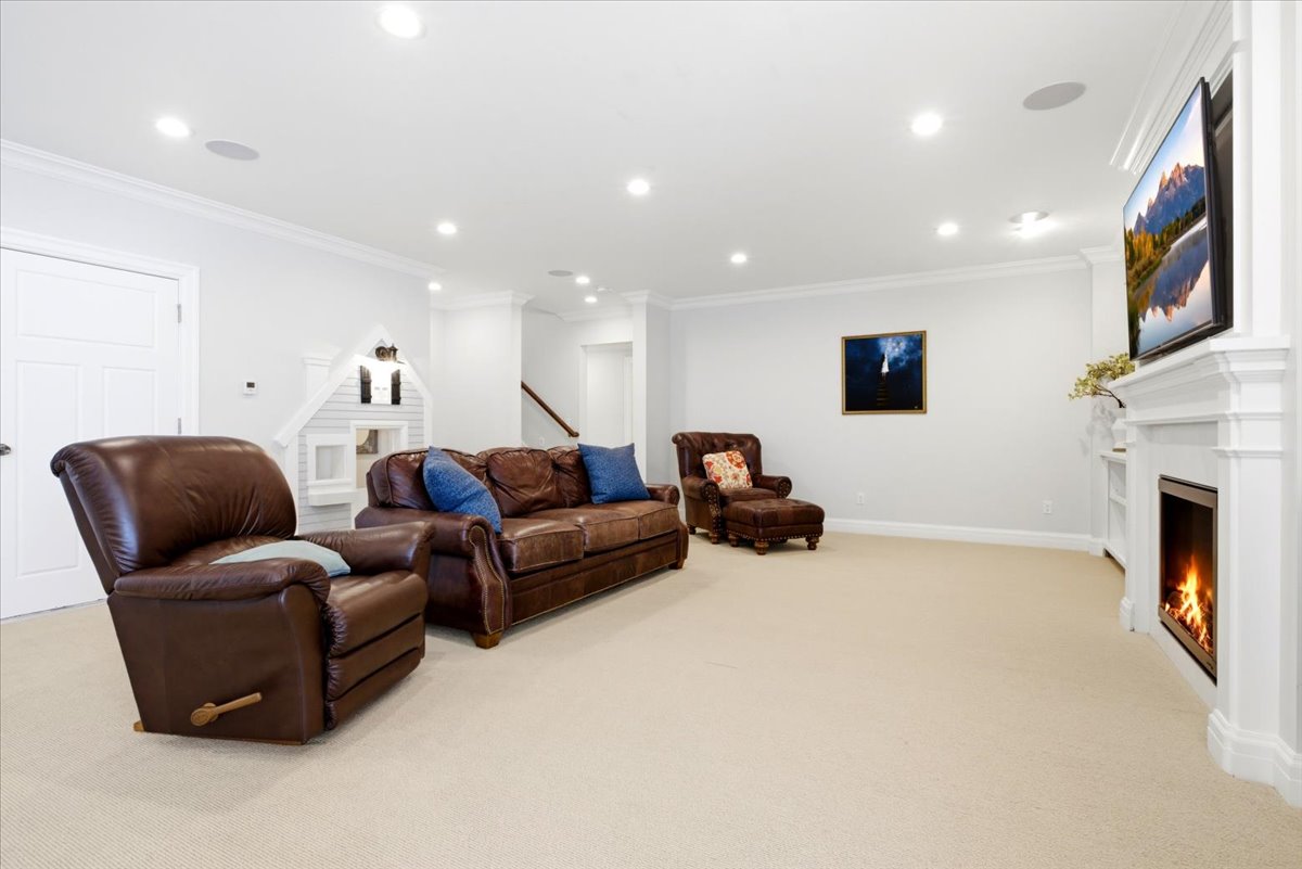 Spacious recreation room featuring recessed lighting, crown molding, a built-in fireplace with a white mantel, and light-toned carpeting