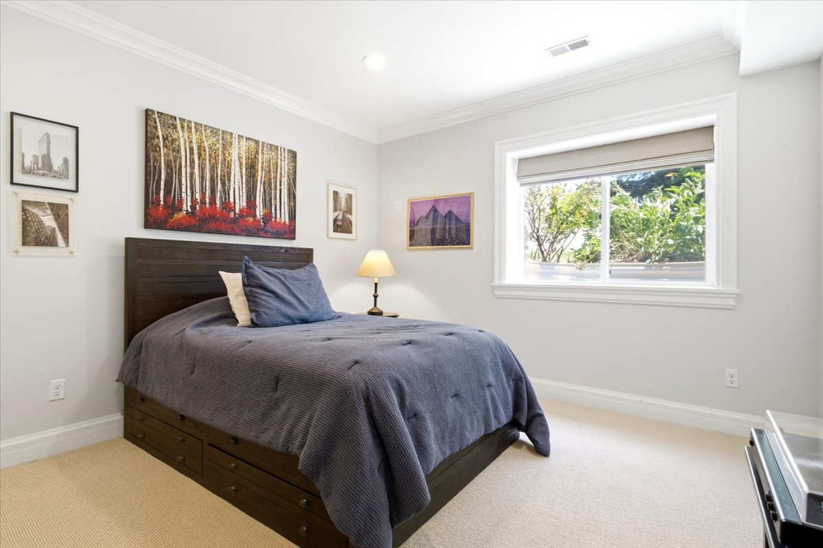 Carpeted bedroom featuring a large window with roller shade, crown molding, recessed lighting, and white baseboards