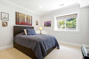 Carpeted bedroom featuring a large window with roller shade, crown molding, recessed lighting, and white baseboards