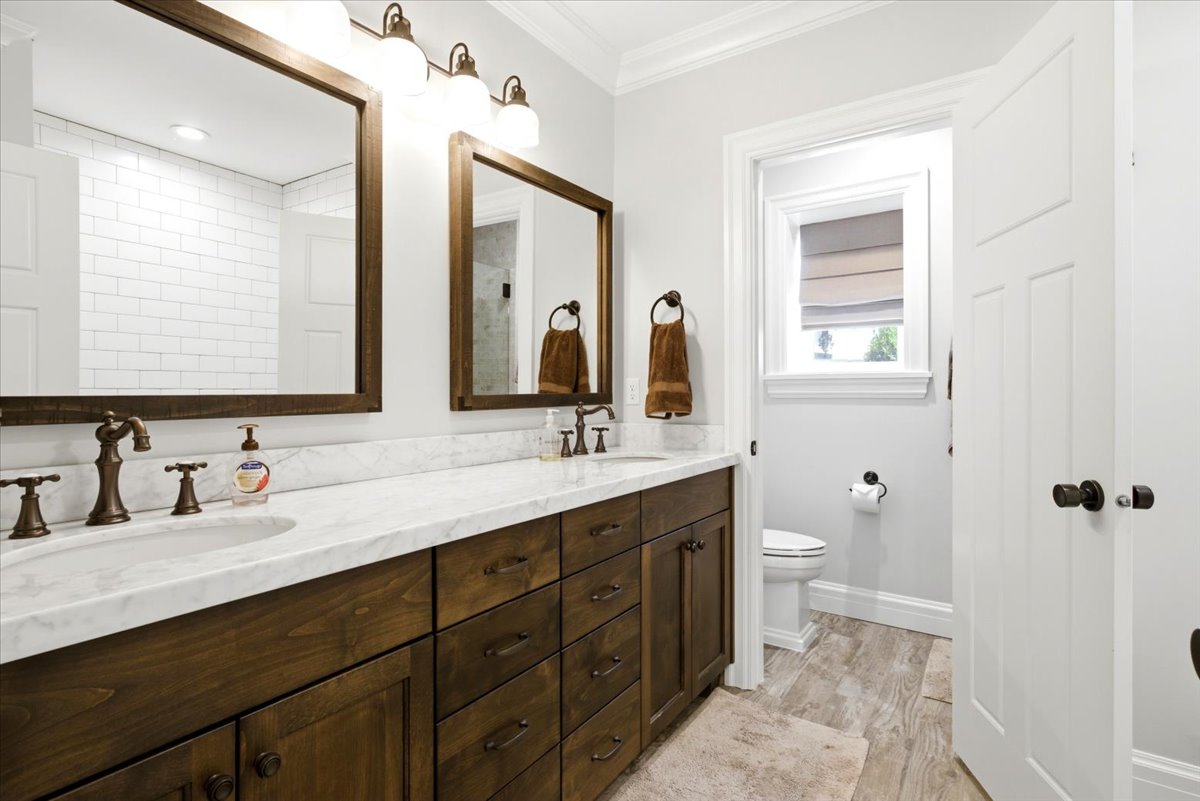 Dual wood-finish vanities with undermount sinks, bronze fixtures, and stone countertops