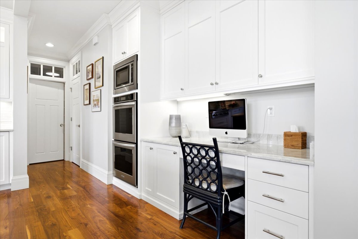 Integrated office nook featuring built-in cabinetry, under-cabinet lighting, a stone countertop, and wood-finish flooring