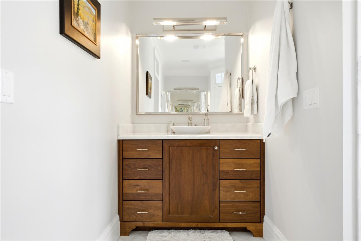 Wood-finish vanity with a vessel sink, stone countertop, and wall-mounted mirror with integrated lighting