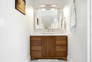 Wood-finish vanity with a vessel sink, stone countertop, and wall-mounted mirror with integrated lighting