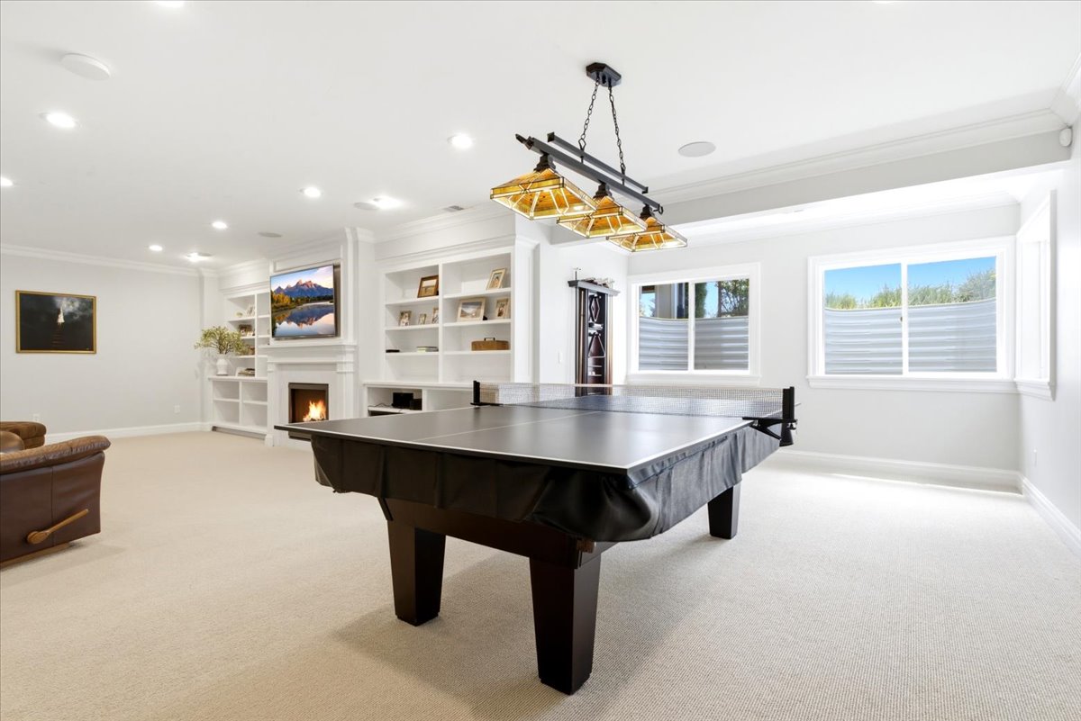 Carpeted recreation room featuring a central game table, recessed lighting, and a linear chandelier