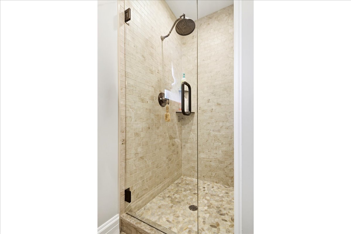 Glass-enclosed shower featuring a rain-style showerhead, a built-in shelf, stone mosaic wall tiling, and pebble flooring