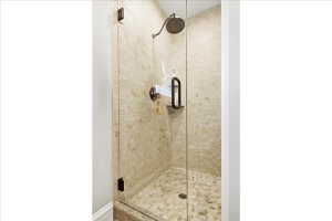 Glass-enclosed shower featuring a rain-style showerhead, a built-in shelf, stone mosaic wall tiling, and pebble flooring