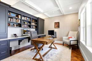 Custom built-in cabinetry with open shelving and closed storage, integrated desk space with a solid surface countertop, coffered ceiling, recessed lighting, and wood-finish flooring