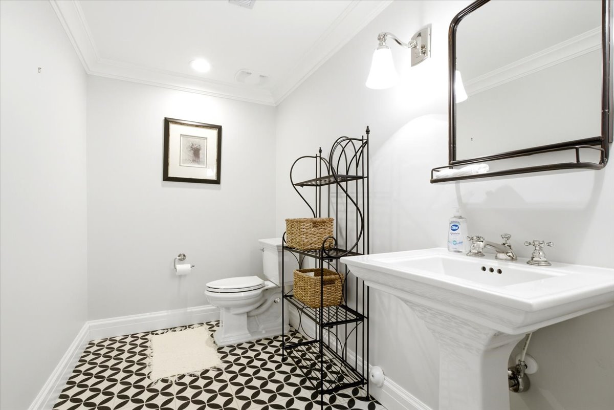 Pedestal sink with polished chrome hardware, black and white patterned floor tiles, recessed lighting, wall-mounted sconce, and crown molding