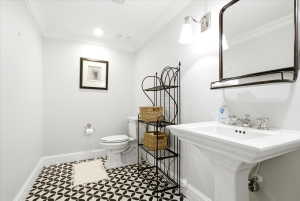 Pedestal sink with polished chrome hardware, black and white patterned floor tiles, recessed lighting, wall-mounted sconce, and crown molding