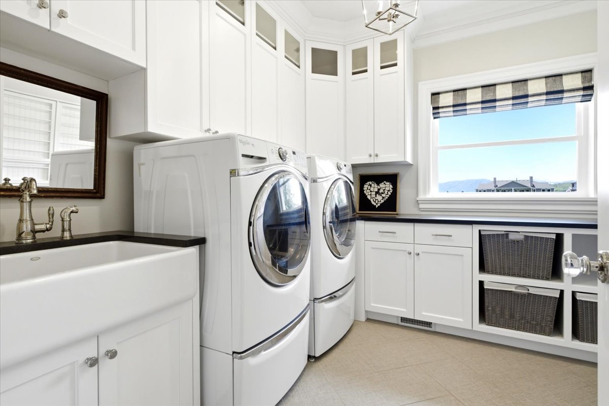 Laundry room featuring white cabinetry, a farmhouse sink with a dark countertop, and light tile flooring