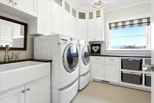 Laundry room featuring white cabinetry, a farmhouse sink with a dark countertop, and light tile flooring