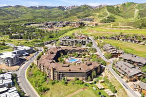 Expansive mountain development featuring a large central building with a pool, multiple surrounding residences, green landscaping, and distant ski slopes