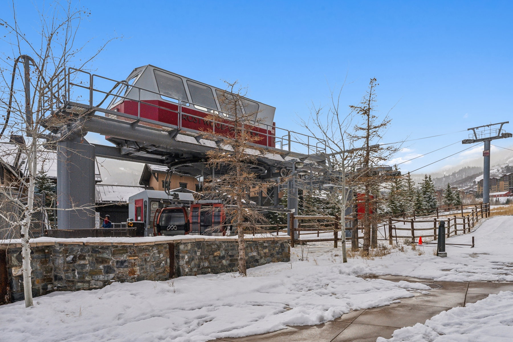 Ski lift station with stone base, supporting multiple ski gondolas, against a backdrop of snow-covered terrain and evergreen trees