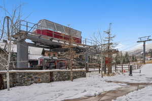 Ski lift station with stone base, supporting multiple ski gondolas, against a backdrop of snow-covered terrain and evergreen trees