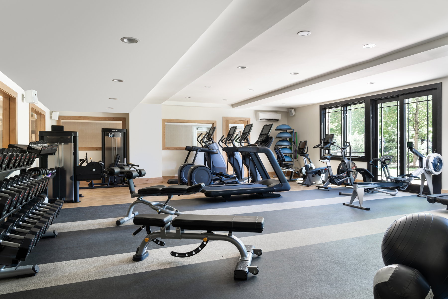 Dedicated fitness space featuring ample natural light, recessed ceiling lighting, a mirrored wall section, and a combination of wood-finish and rubber flooring