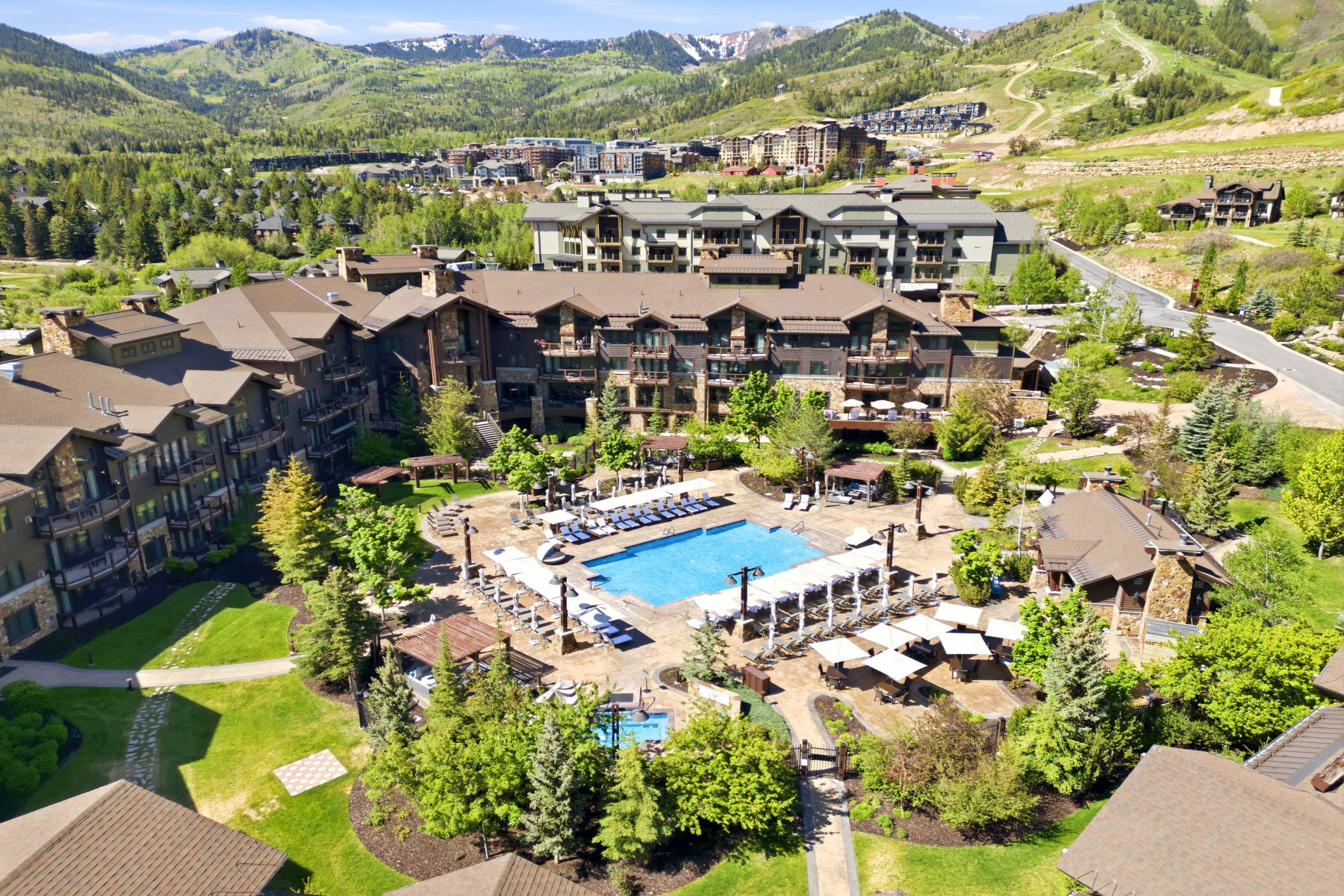 Central resort-style pool area with surrounding lounge seating, mature landscaping, and mountain backdrop