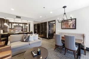 Open concept living space featuring a kitchen with dark wood cabinetry and pendant lighting, a dining area with a linear chandelier, and a carpeted floor