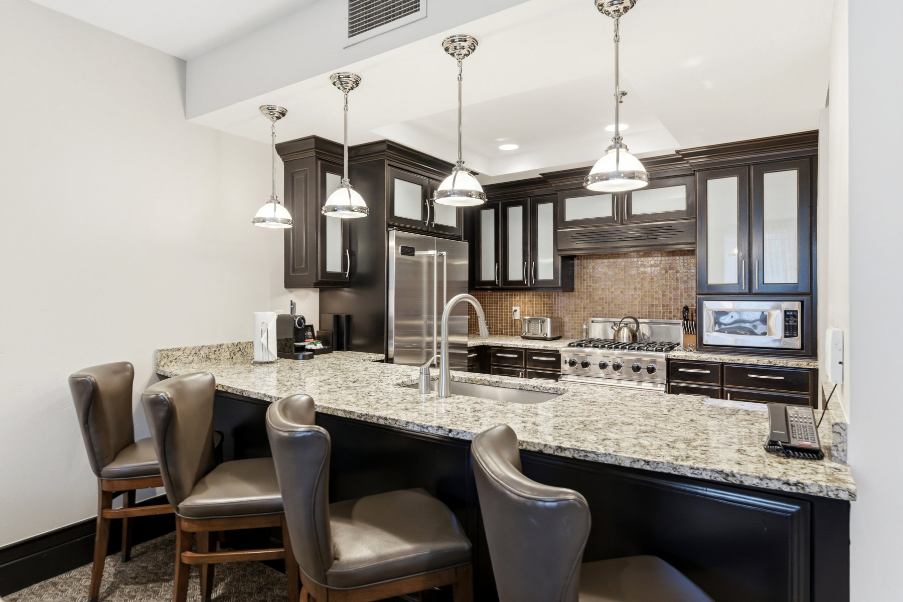 Kitchen featuring dark cabinetry with glass-front uppers, light-toned stone countertops, and a full-size stainless steel range