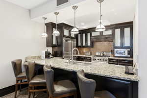 Kitchen featuring dark cabinetry with glass-front uppers, light-toned stone countertops, and a full-size stainless steel range