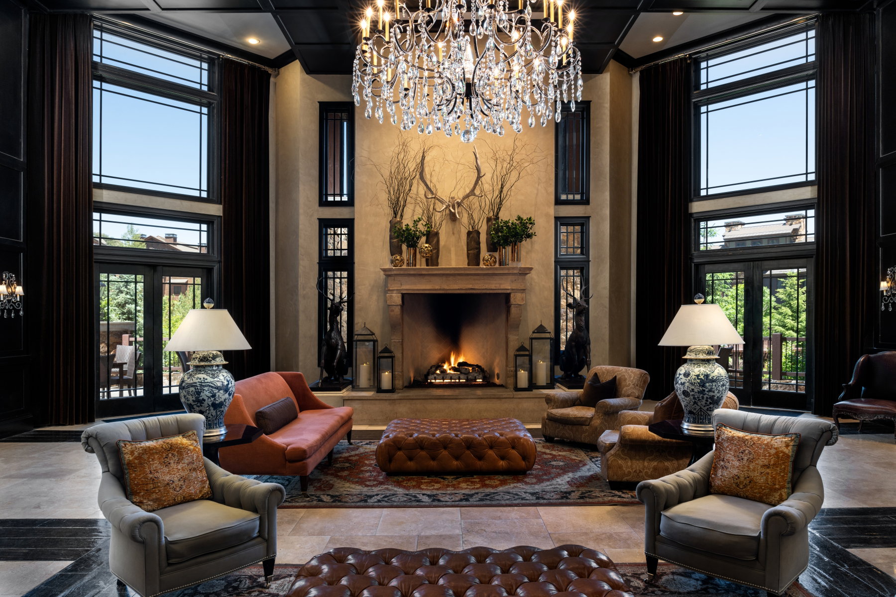 Grand living space featuring a large chandelier, a stone fireplace, and multiple tall windows with transoms