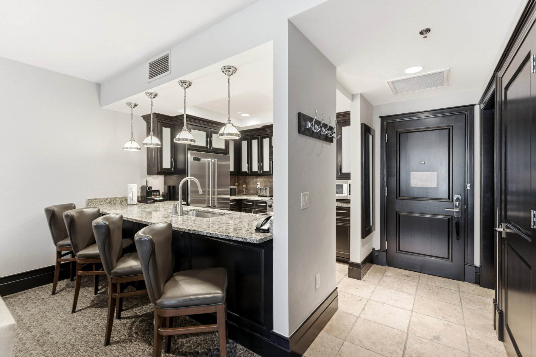 Kitchen with a granite countertop breakfast bar, stainless steel appliances, dark wood cabinetry, and pendant lighting