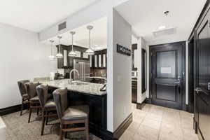 Kitchen with a granite countertop breakfast bar, stainless steel appliances, dark wood cabinetry, and pendant lighting