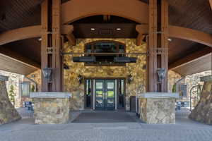Stone and wood-beam porte-cochère entrance featuring double glass-paneled doors, arched window, and integrated outdoor lighting fixtures