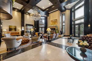 Grand foyer featuring a coffered ceiling, a large crystal chandelier, and a fireplace with a decorative mantel