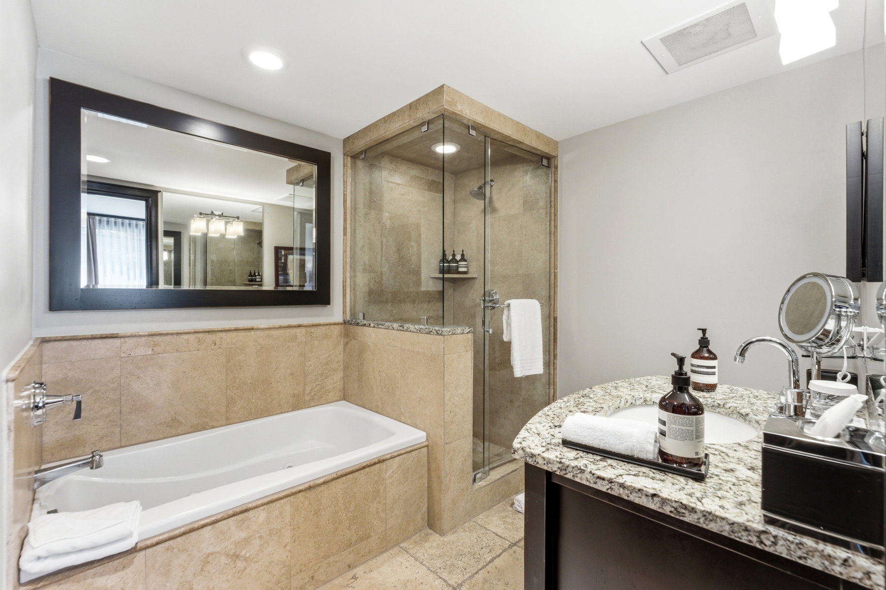 Bathroom featuring a built-in soaking tub with stone surround, a glass-enclosed shower with stone tiling, a vanity with a granite countertop and integrated sink, a large framed mirror, and recessed lighting