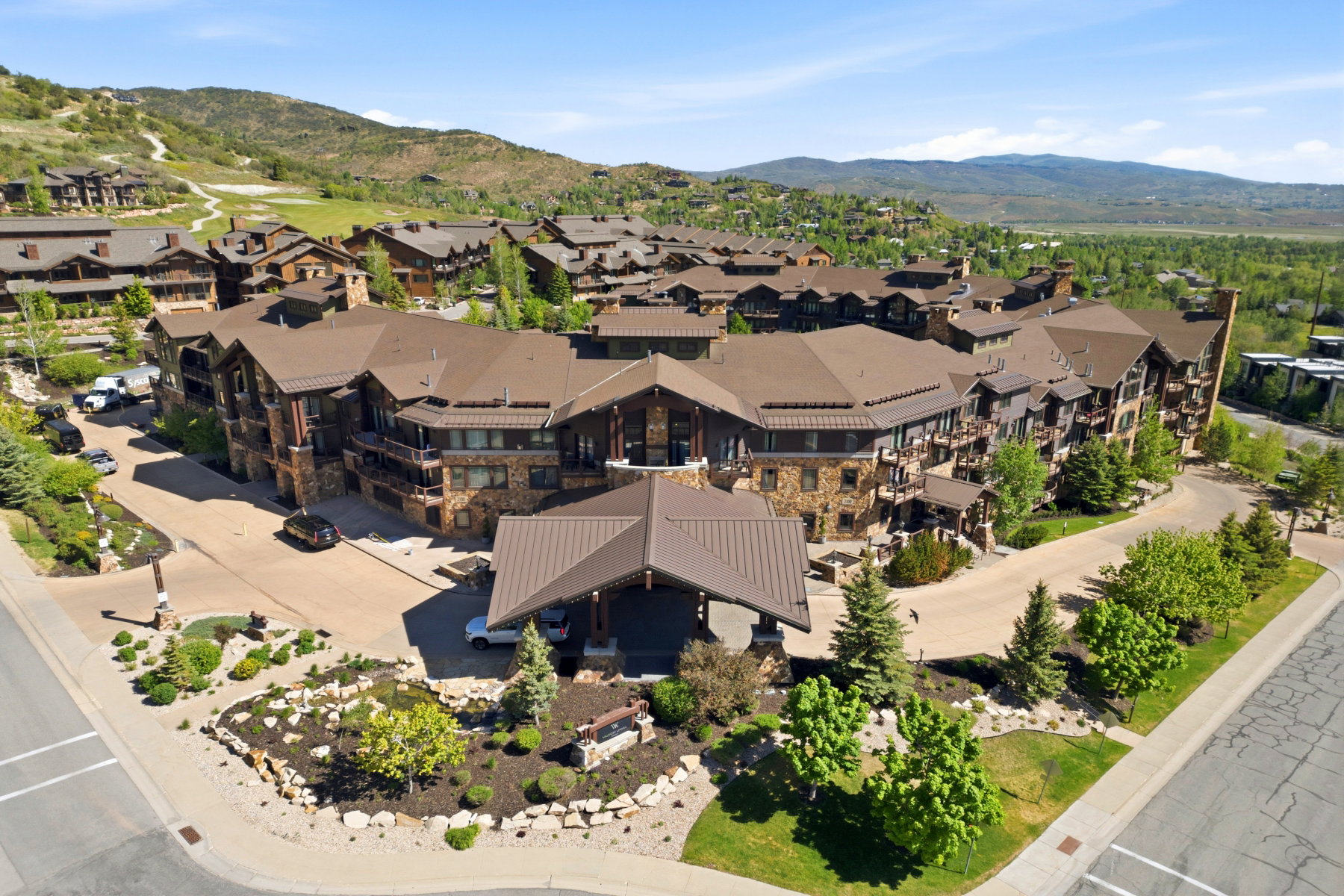 Expansive multi-story building featuring stone and wood siding, multiple balconies, a covered entryway, and mature landscaping