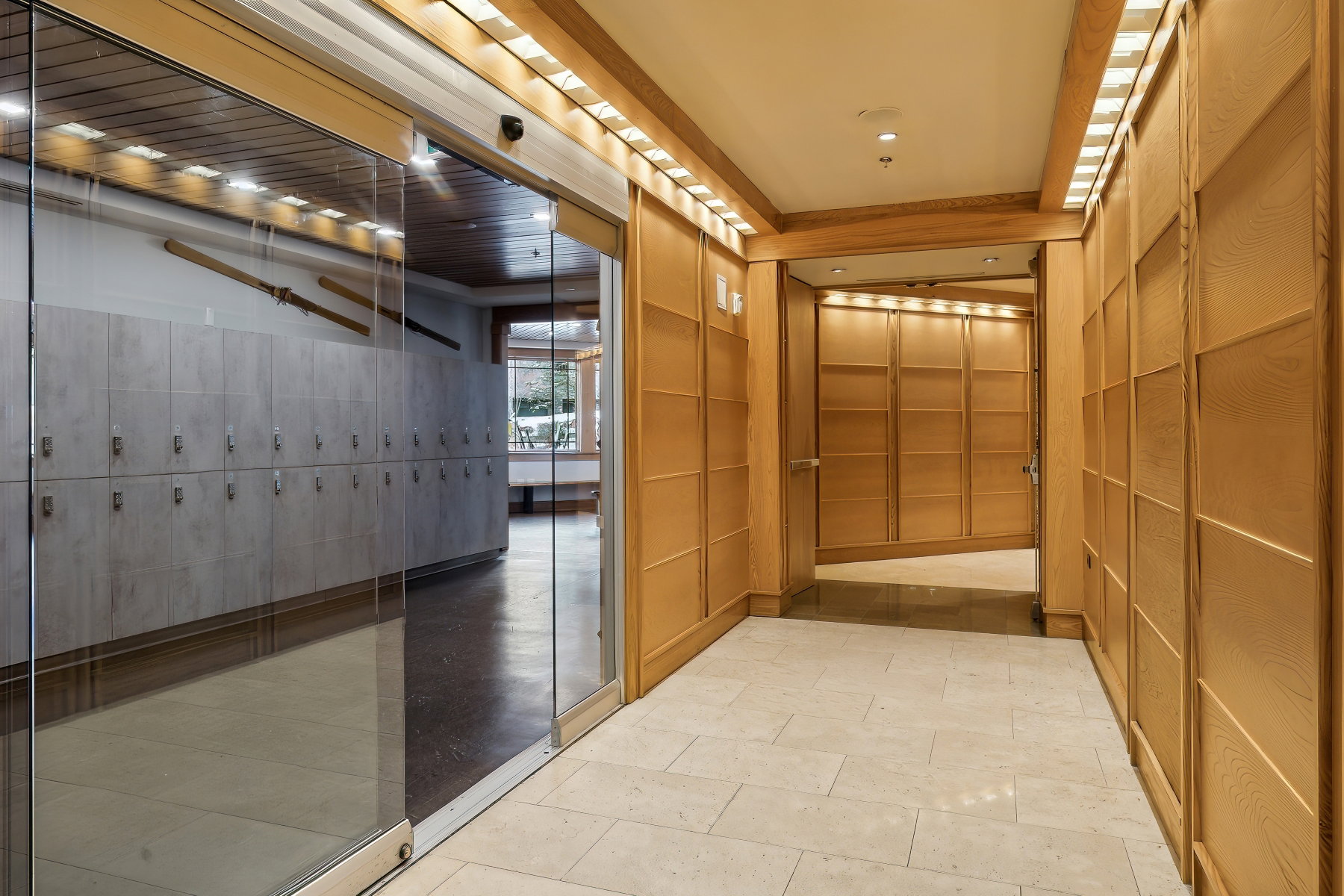 Corridor featuring light wood paneling, tiled flooring, recessed lighting, and a glass-paneled sliding door
