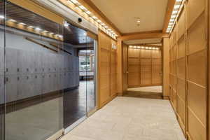 Corridor featuring light wood paneling, tiled flooring, recessed lighting, and a glass-paneled sliding door