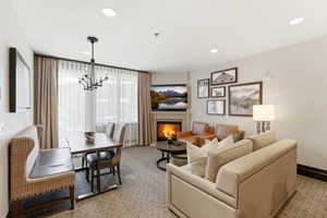 Open-concept living area featuring a corner fireplace, recessed lighting, expansive windows with drapery, and a dining area with a chandelier