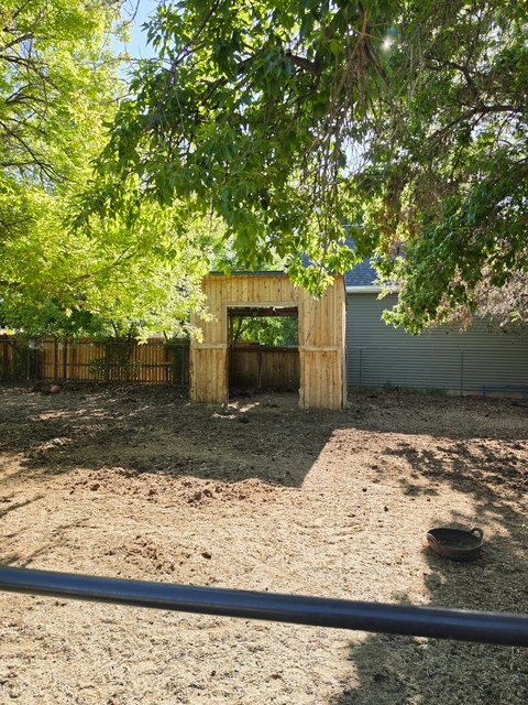 Outdoor structure featuring natural wood siding and an open entryway, situated within a fenced area