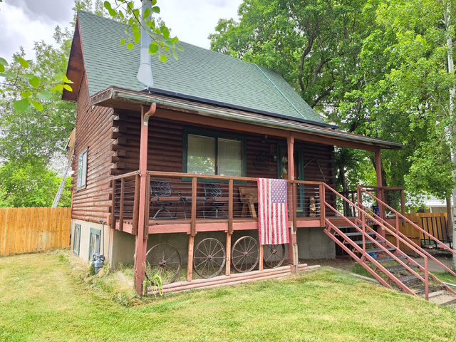 Log cabin exterior featuring a covered front porch, green shingle roof, and wooden railing