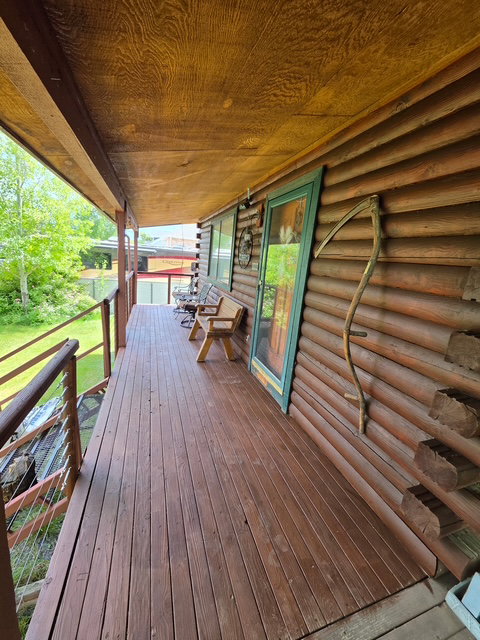 Spacious front porch featuring natural wood-finish decking, cable railing, exposed wood-grain ceiling, and a log-cabin style exterior wall