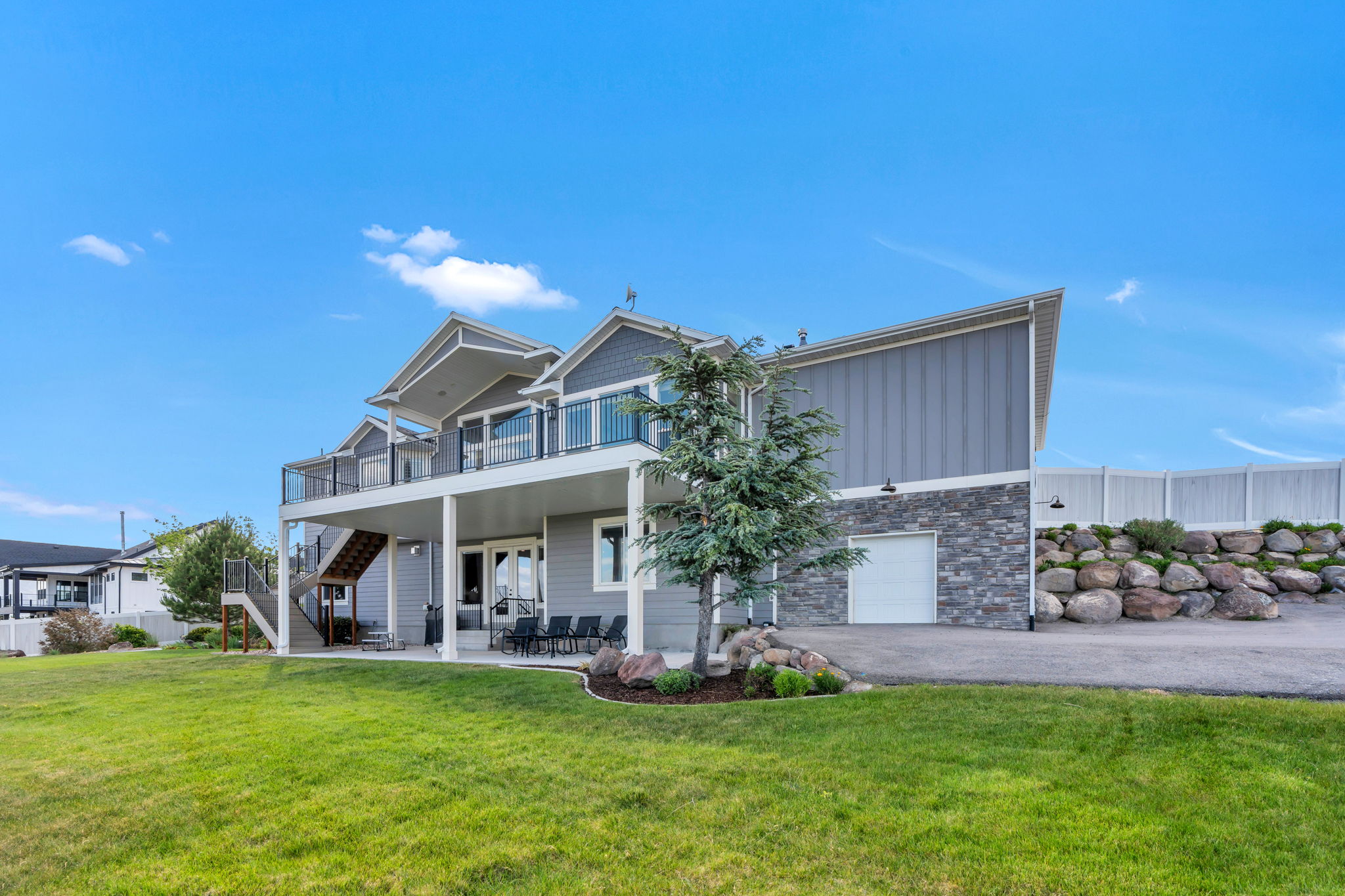 Multi-level residence featuring a spacious rear lawn, an upper deck with glass railings, and a lower covered patio