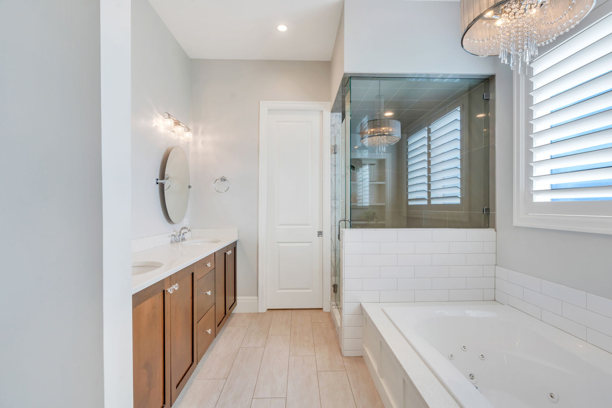 Contemporary bathroom featuring a double vanity with stone countertops, a jetted soaking tub, and a glass-enclosed shower