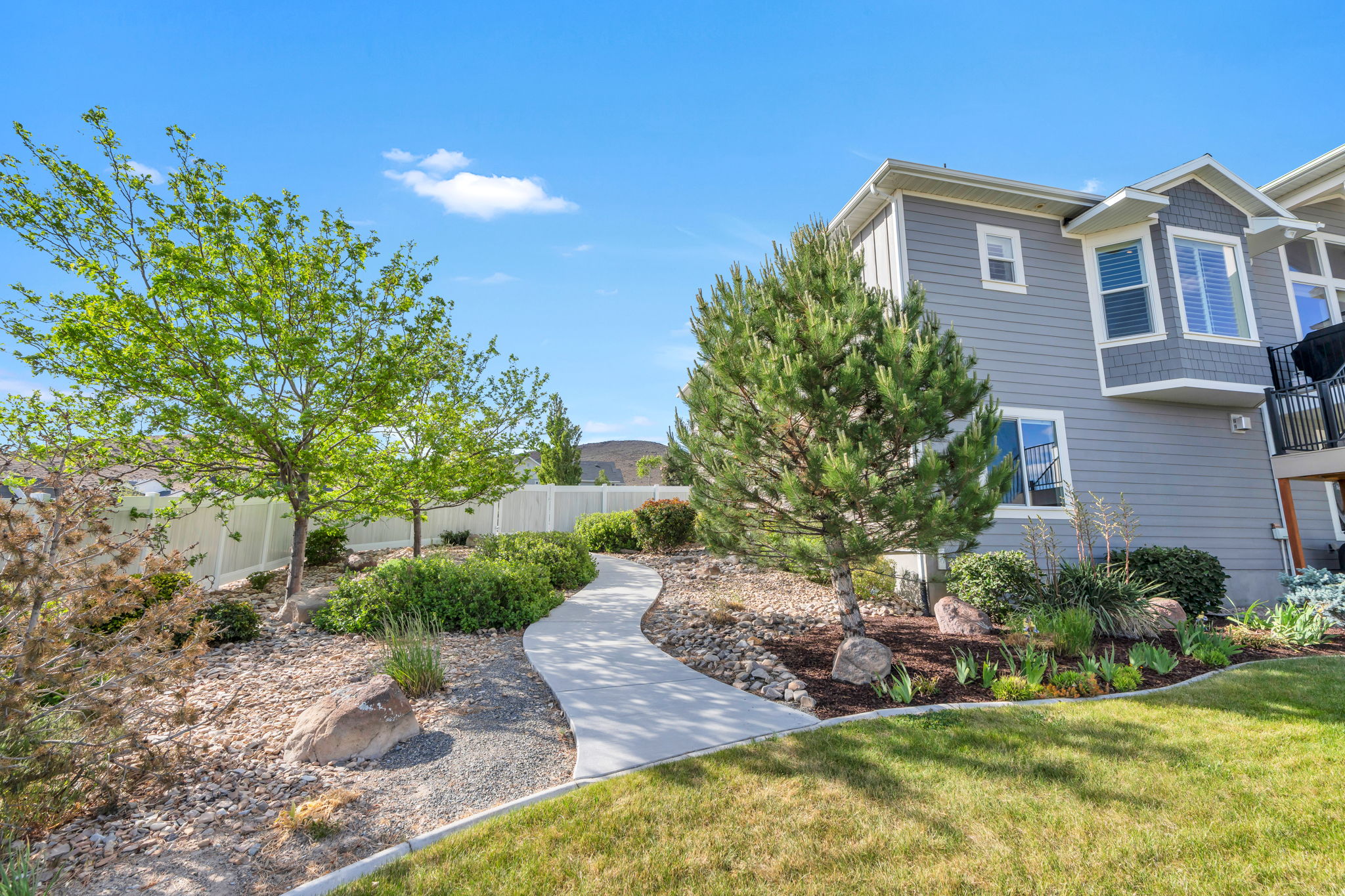 Manicured landscaping with a paved walkway, established trees, and decorative rock features