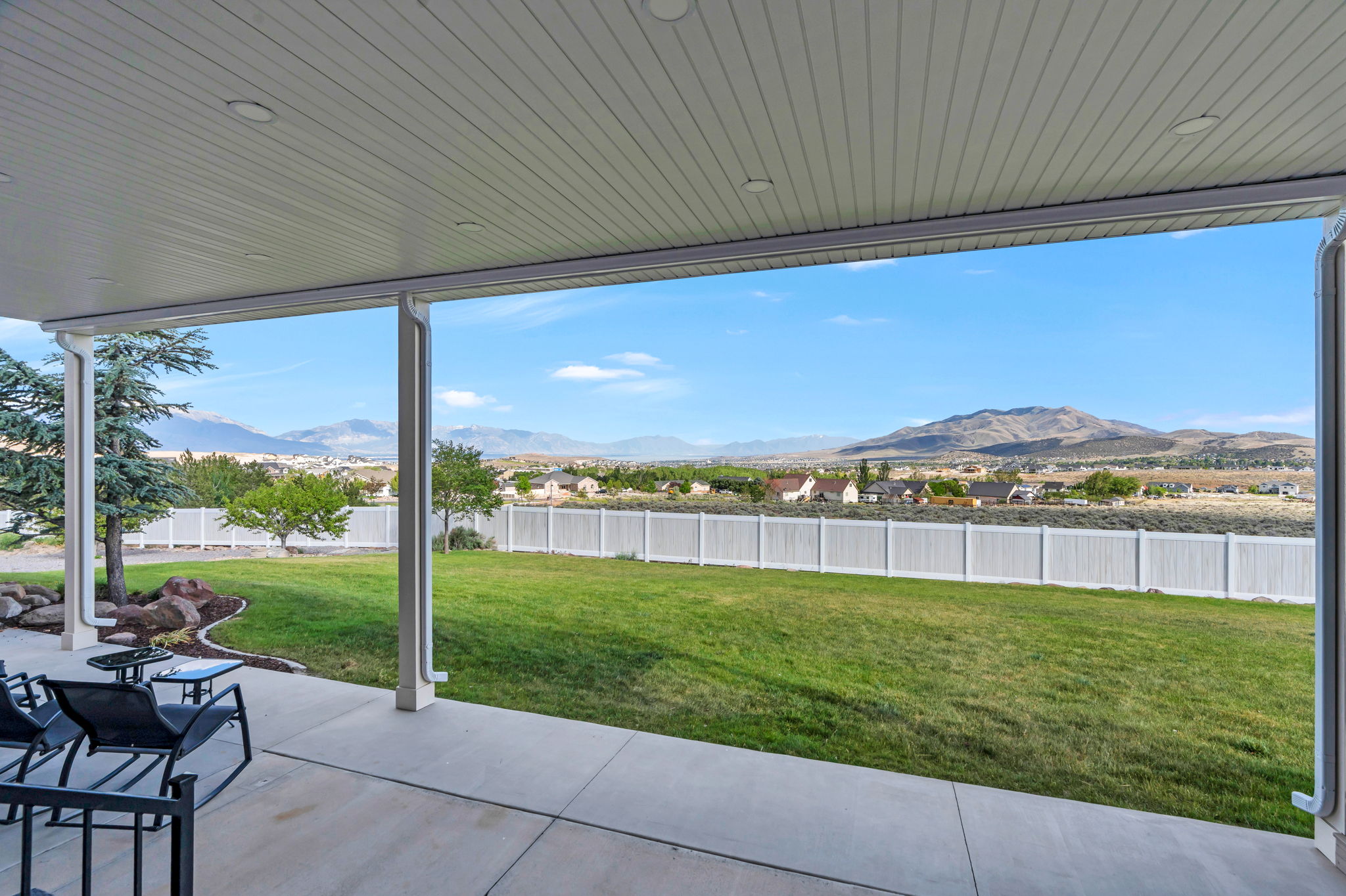 Covered patio with recessed lighting, concrete flooring, expansive green lawn, and white privacy fencing