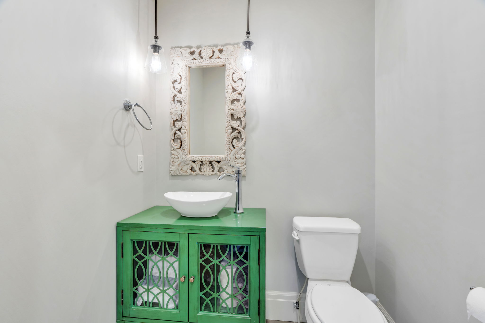 Powder room featuring a green vanity with decorative cabinet doors, a vessel sink, and a carved ornate mirror