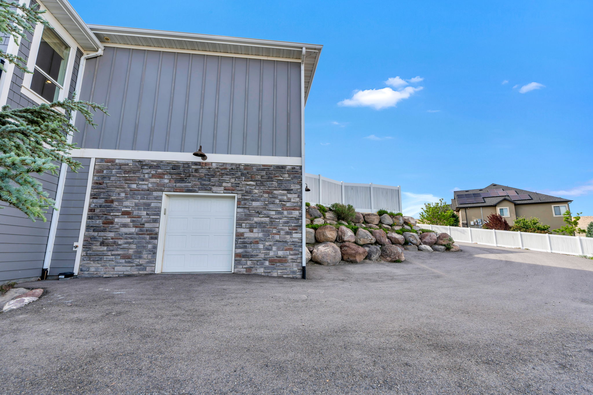 Exterior featuring gray horizontal siding, vertical siding, stone veneer, and a white garage door