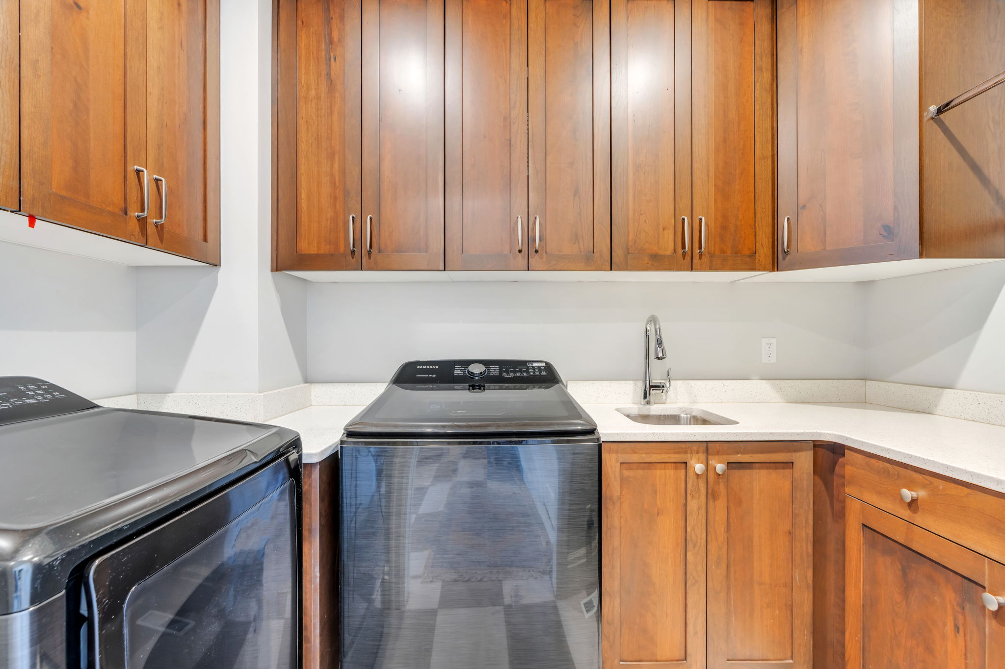 Laundry room featuring wood cabinetry, light countertops, a utility sink with a gooseneck faucet, and a built-in hanging rod
