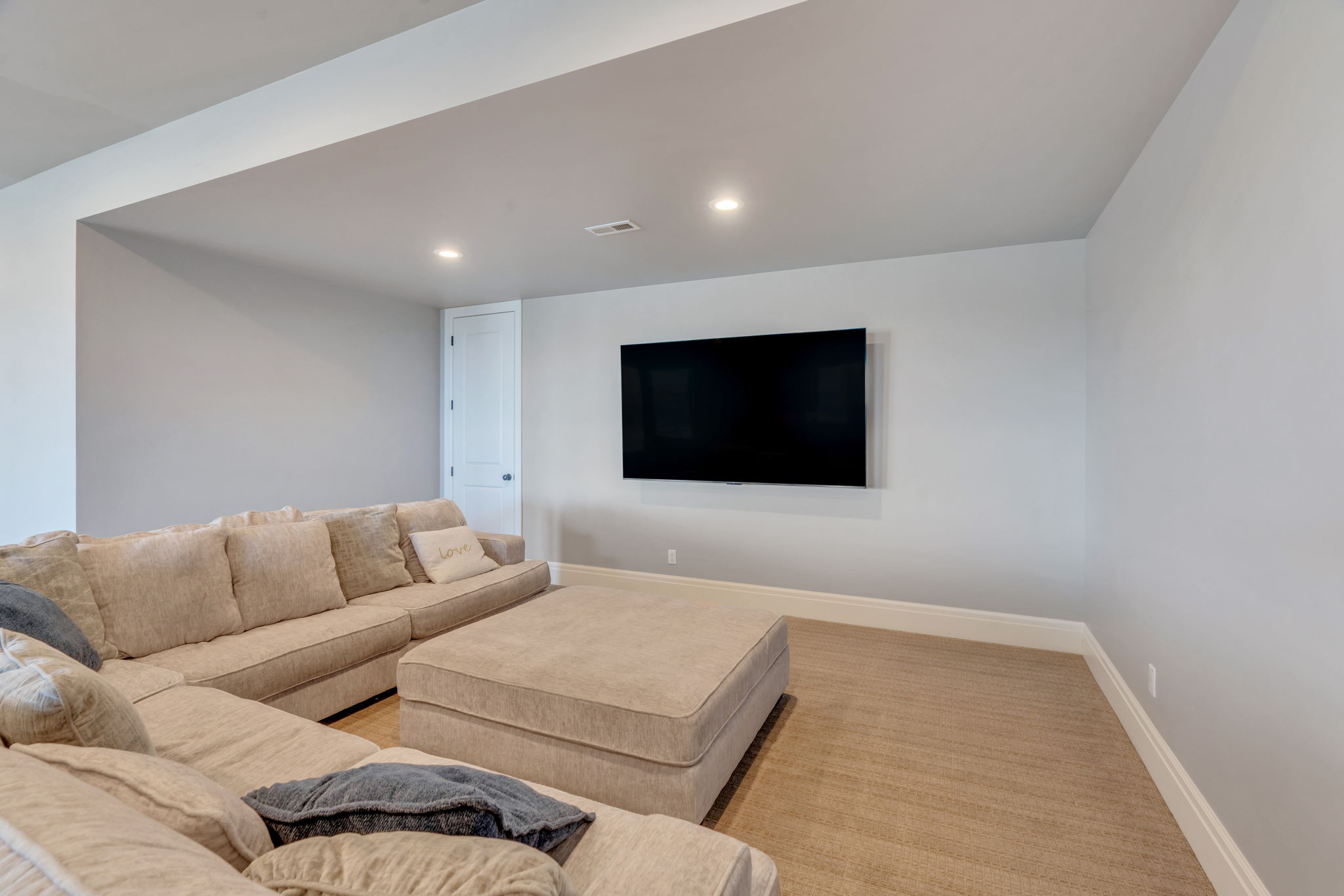 Spacious media room featuring recessed lighting, light wood-finish flooring, a wall-mounted display area, and a white paneled door