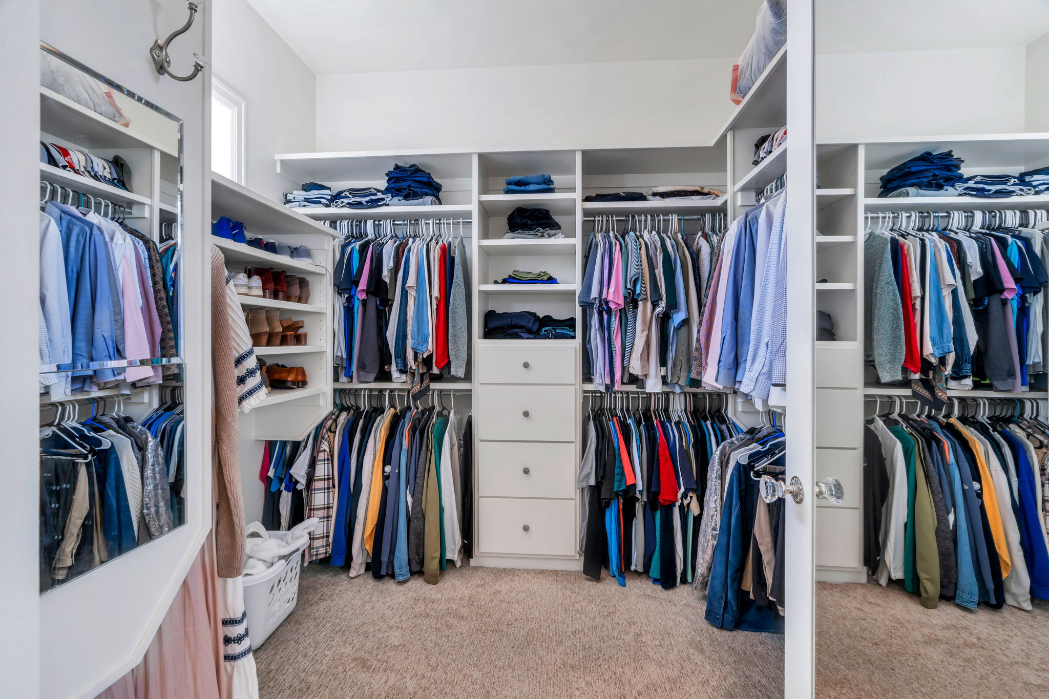 Walk-in closet featuring built-in white cabinetry, multiple hanging rods, integrated shelving, central drawer stacks, and soft pile carpeting