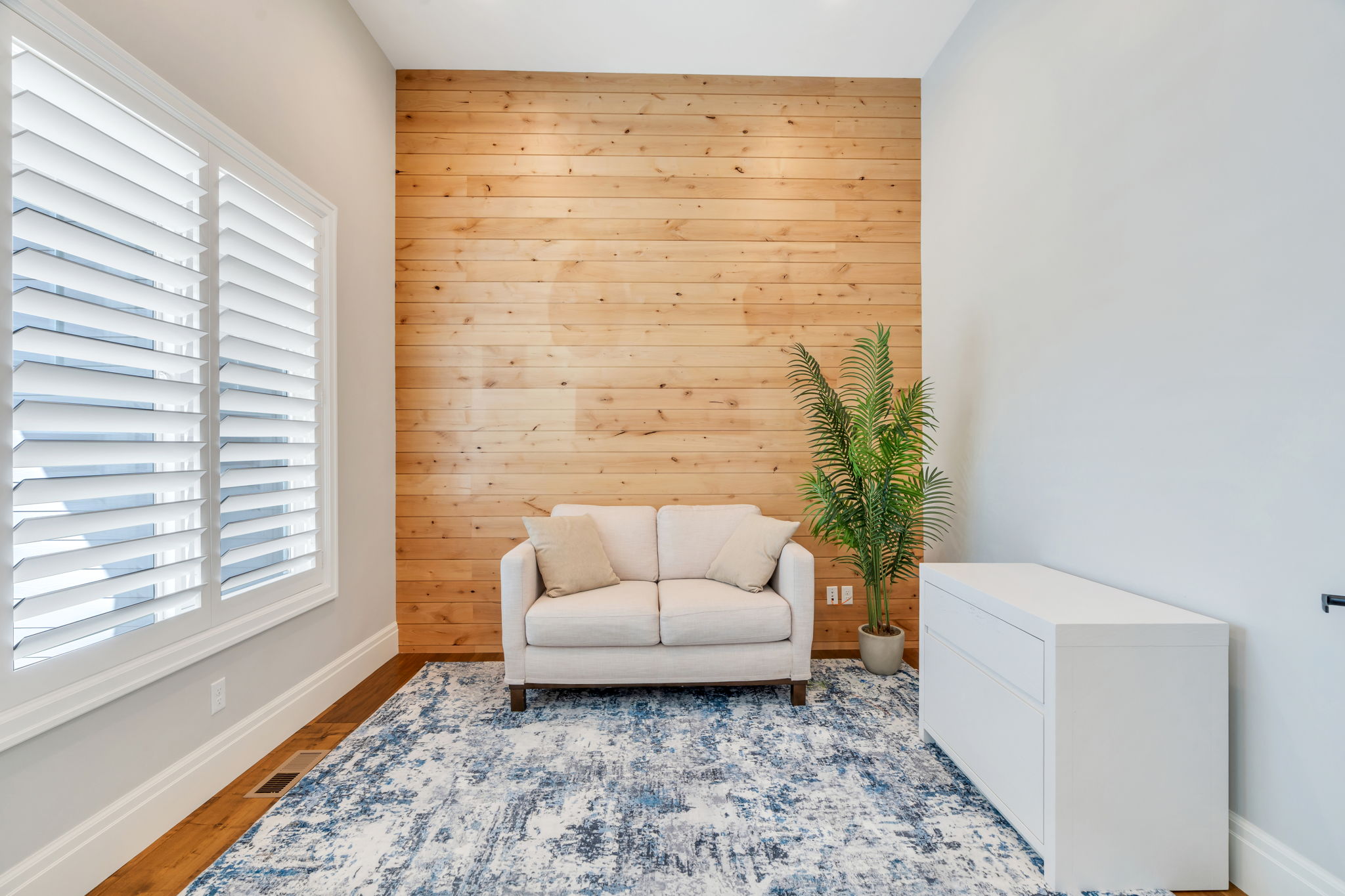 Accent wall featuring horizontal wood paneling and recessed lighting, window with white plantation shutters, and wood-finish flooring