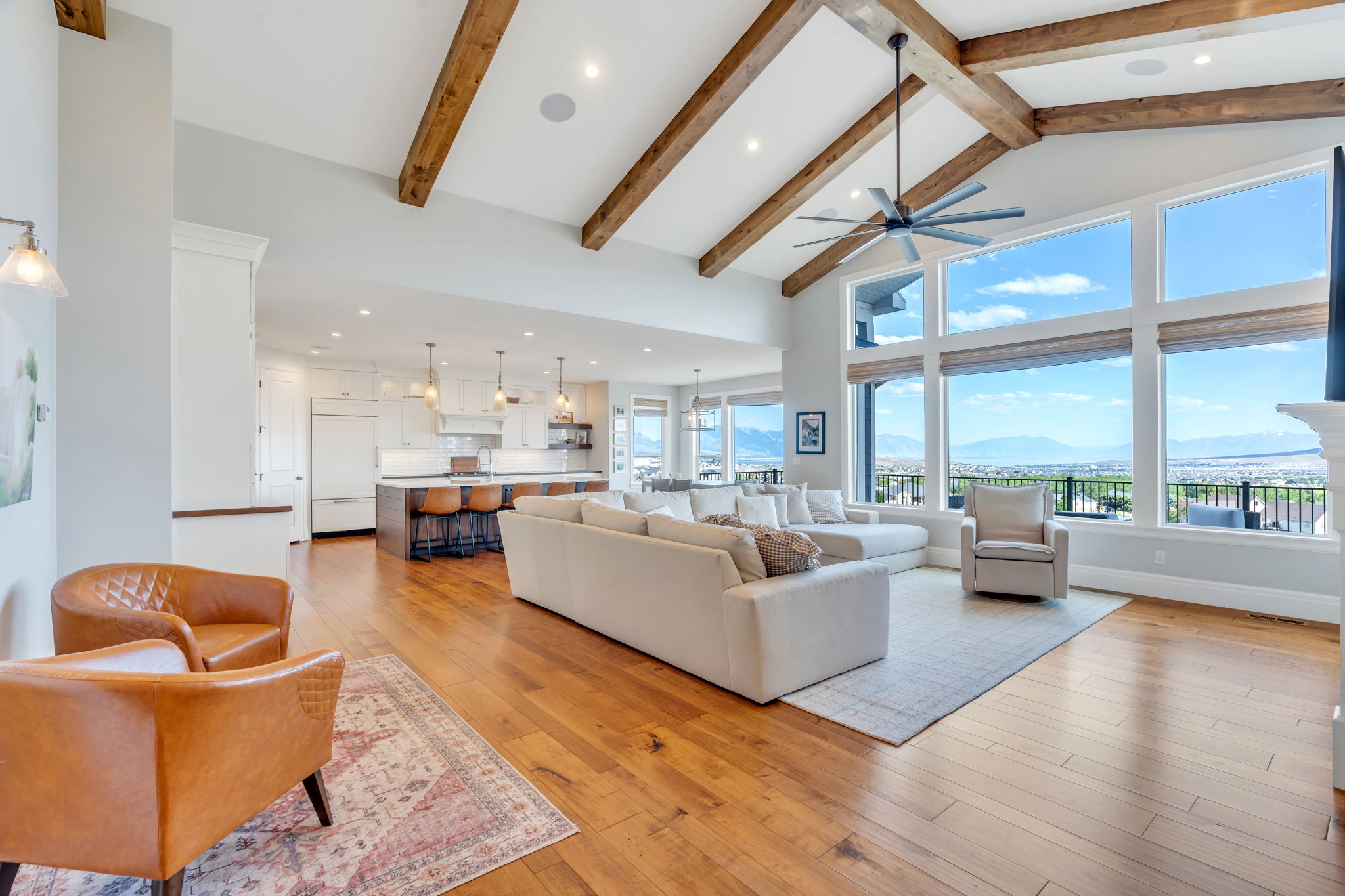 Expansive living area featuring vaulted ceilings with exposed wood beams, a large wall of windows, and wood-finish flooring