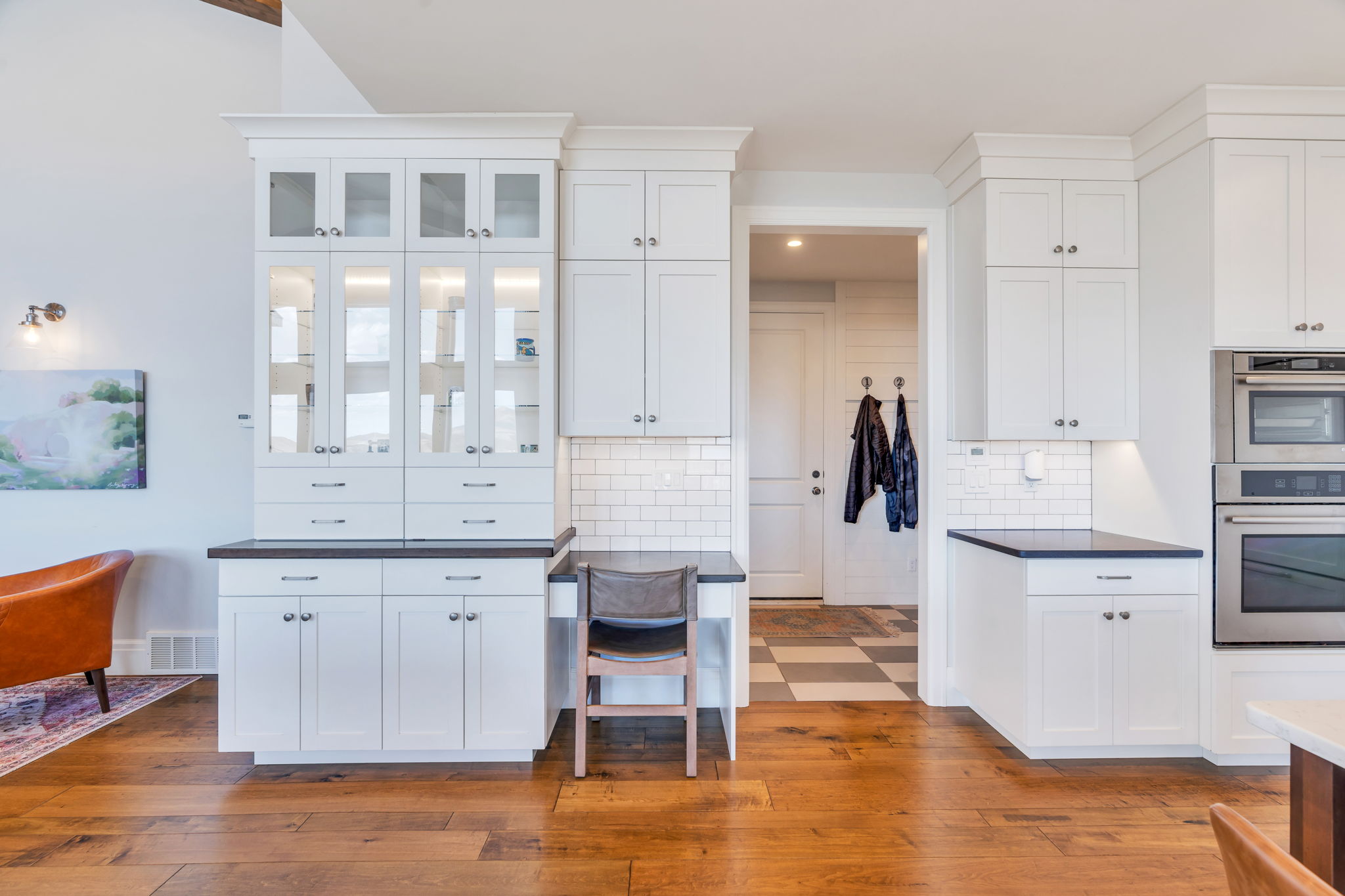 White shaker cabinetry with glass-front uppers, dark countertops, a subway tile backsplash, integrated stainless steel appliances, and wood-finish flooring
